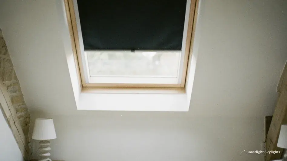 Roof window with a black blackout blind drawn in a white sloping ceiling