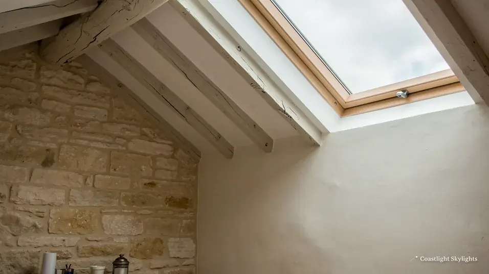Loft room with a roof window in the sloping ceiling and an exposed stone wall