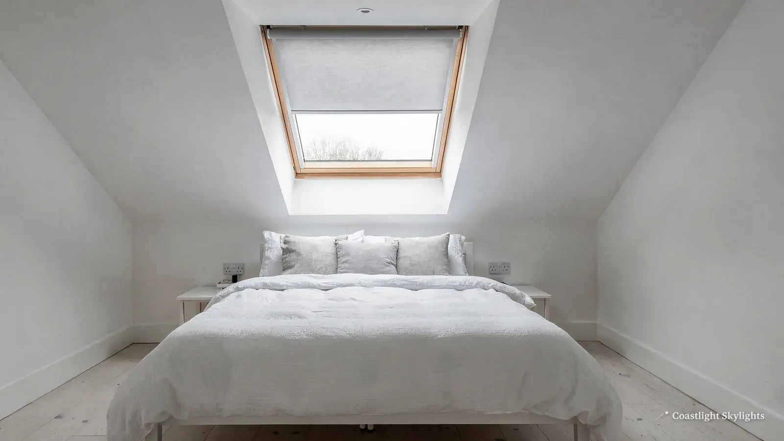 White loft bedroom with a bed beneath a roof window in the sloping ceiling