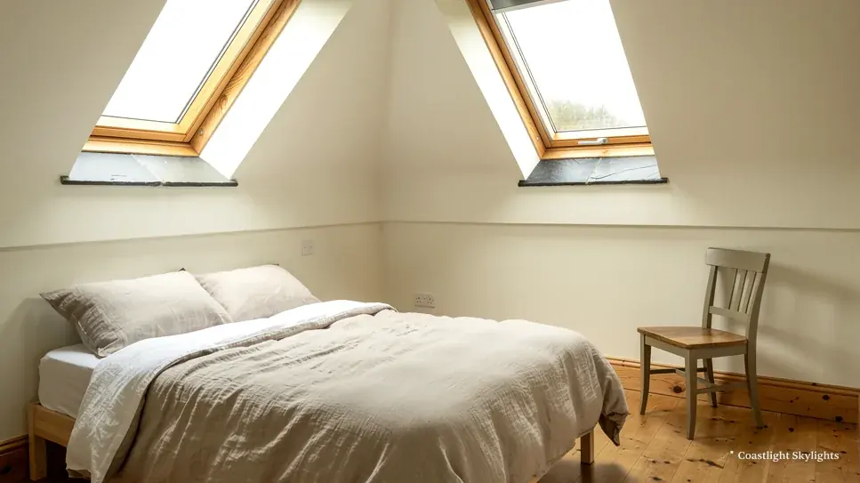 Loft bedroom with a bed beneath two roof windows in the sloping ceiling
