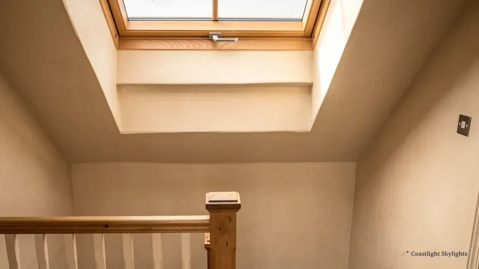 Roof window above a staircase and timber banister in a cream painted loft