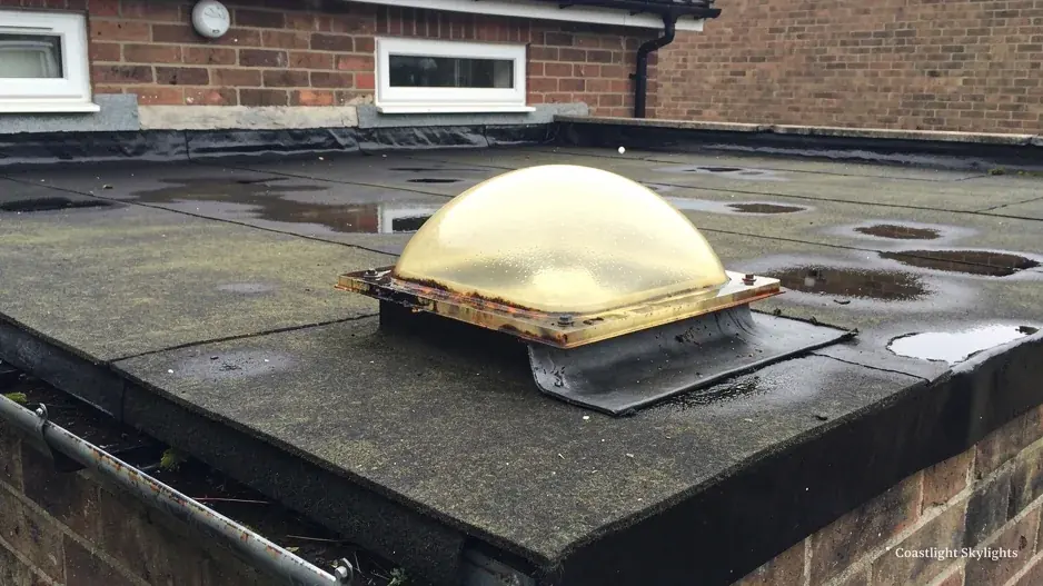 Yellowed plastic dome rooflight on a dark flat roof beside a gutter