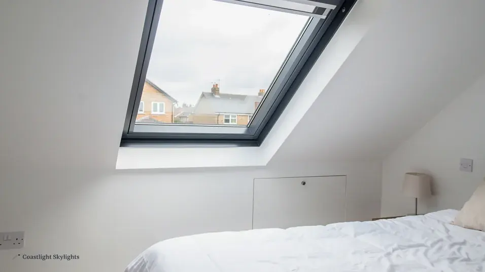 Loft bedroom with a bed beneath a roof window looking out to the sky