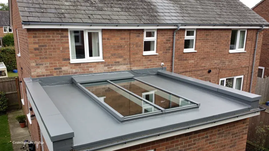 Flat grey roof with an opening rooflight beside a brick house