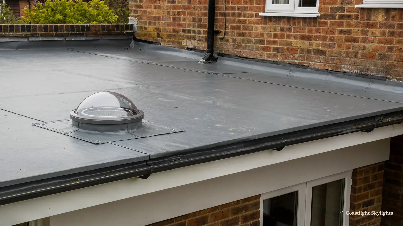 Round sun tunnel dome on a grey flat roof beside a glazed extension