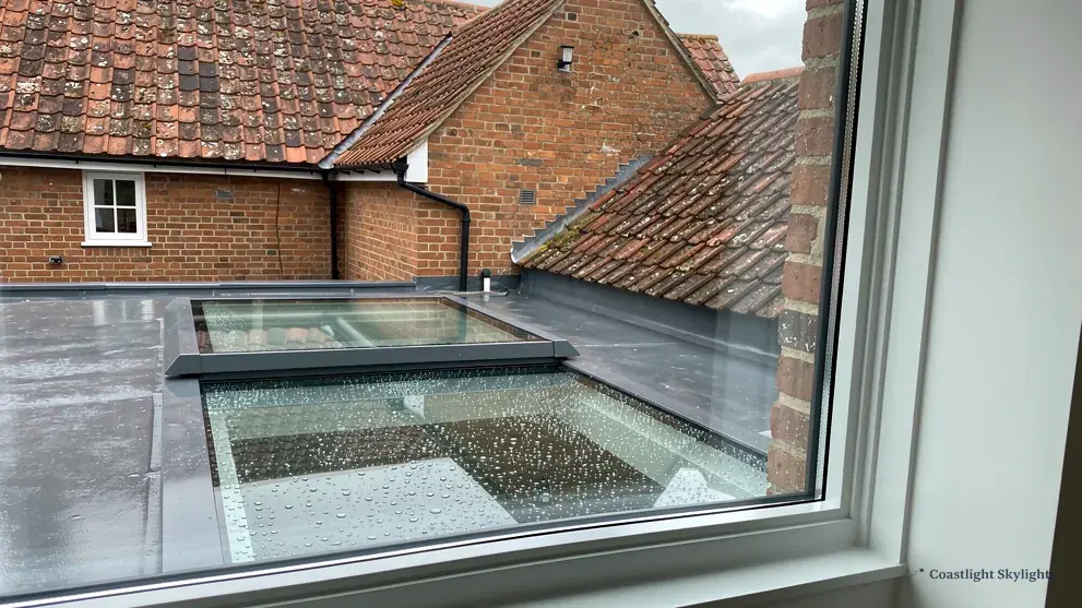 Frosted glass rooflight on a kerb in a grey flat roof beside a brick house