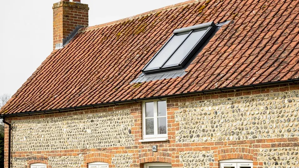 Flint and brick cottage with a slim roof window set into its clay tiled roof