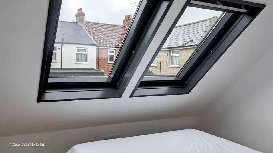 Two black-framed roof windows above a bed seen from inside a loft room
