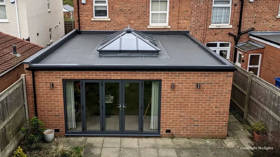 Brick extension with a glass pyramid lantern on its flat roof and folding doors