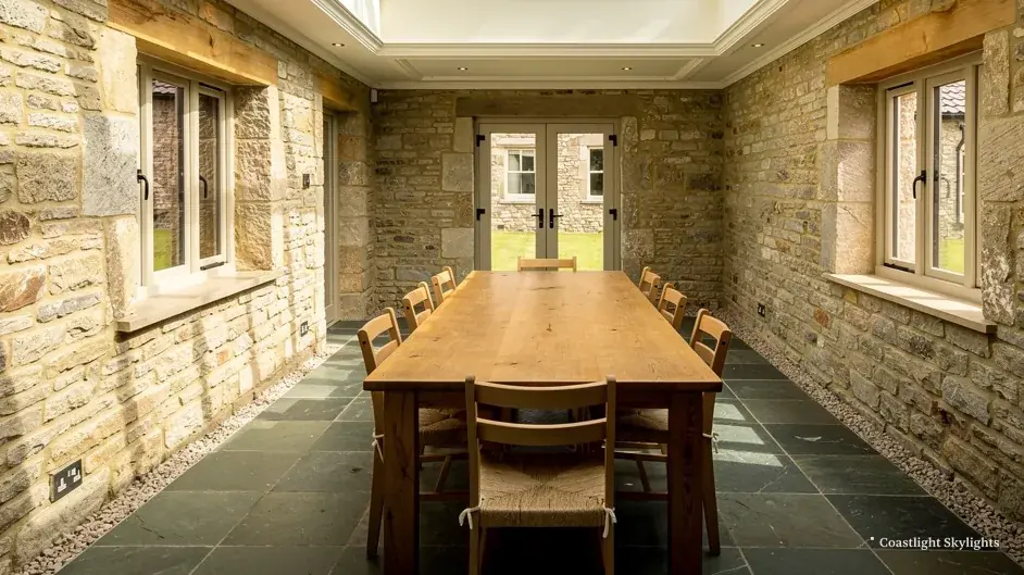 Stone walled garden room with a long dining table and glazed doors at the far end