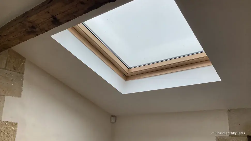 Roof window with a timber frame seen from inside a plain room