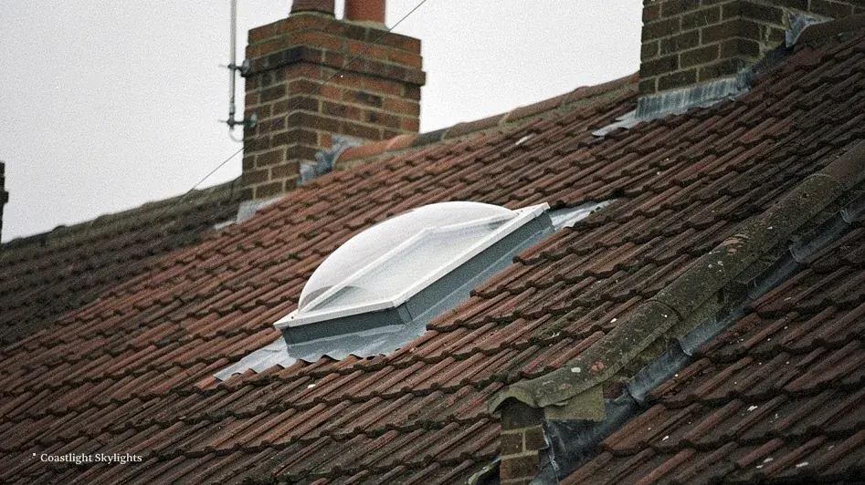 Round sun tunnel dome set into a clay tiled roof beside a brick chimney