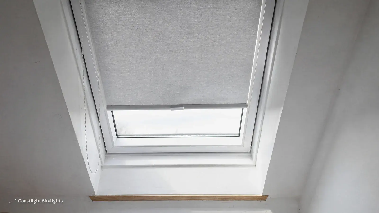 Roof window with a grey roller blind in a white sloping ceiling