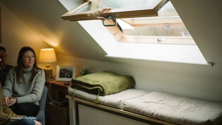 Two people sitting on a loft bed beneath a roof window in a sloping ceiling
