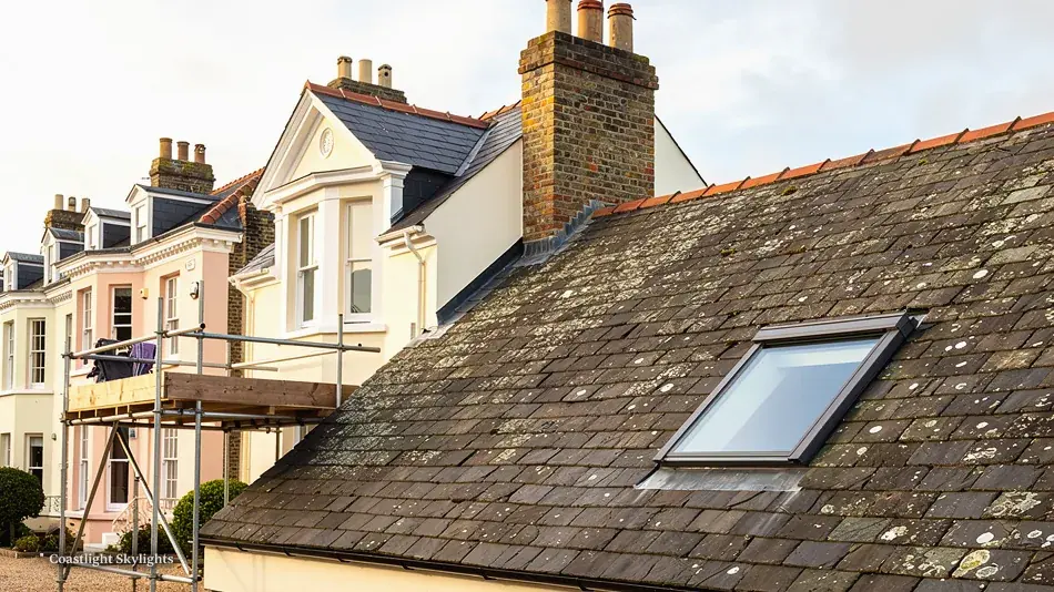 Scaffold at the eaves of an old tiled roof with a roof window in the slope
