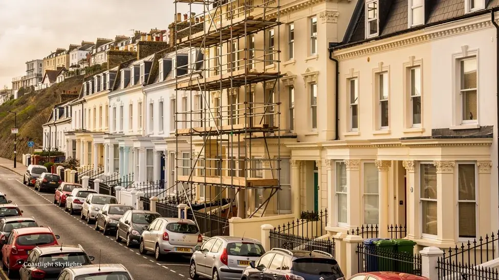 Scaffold against the front of a tall rendered terraced house on a narrow street