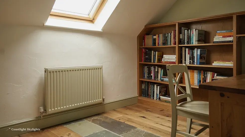 Loft study with bookshelves, a radiator and a roof window above